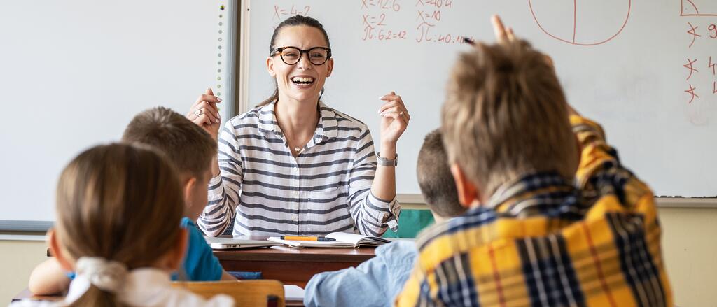 Lehrerin sitzt am Pult vor der Klasse