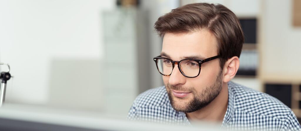 Mann mit Brille sitzt vor Bildschirm