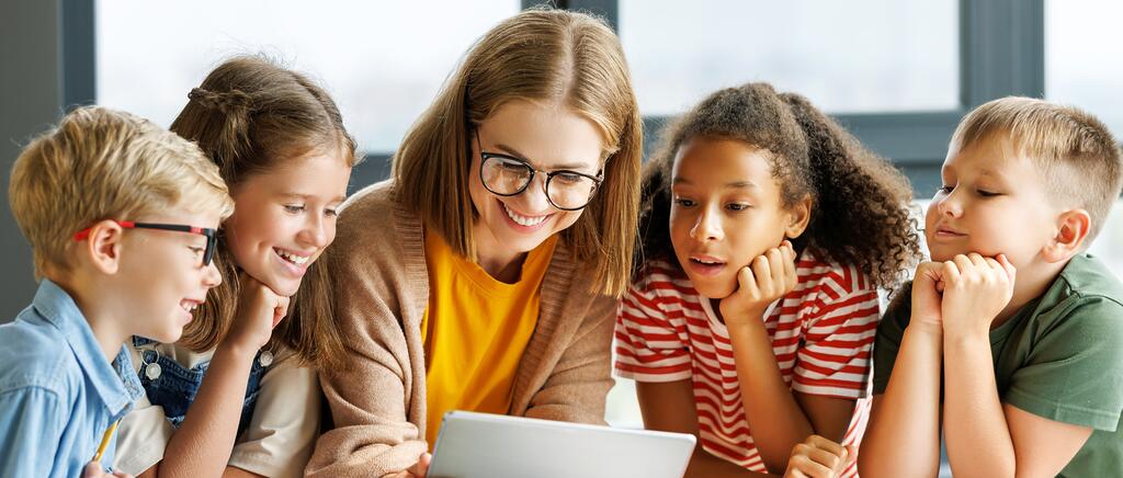 Eine Lehrerin zeigt vier Schülerinnen und Schülern Inhalte auf einem Tablet.